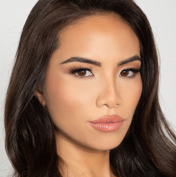 Female model with dark brown hair wearing Reese Robert Beauty's Faux Fur 2D Feather Effect lashes on light gray background